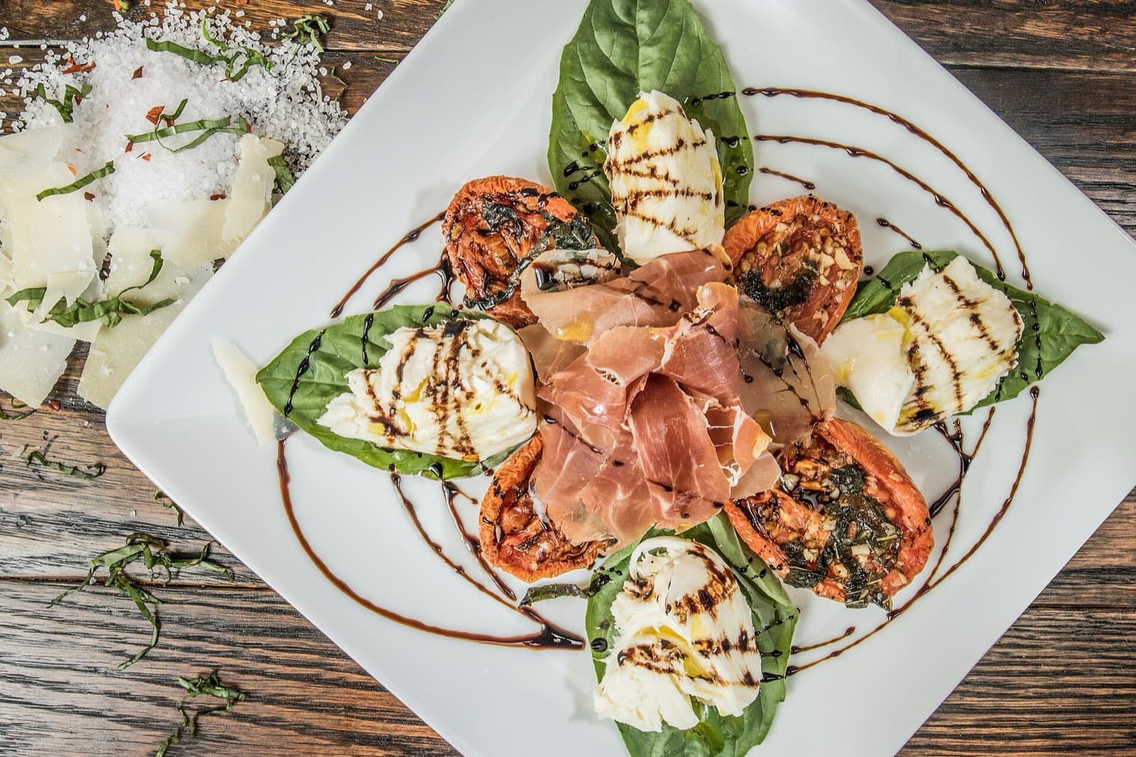 Mozzarella, cured ham and roasted tomatoes with basil on a white plate