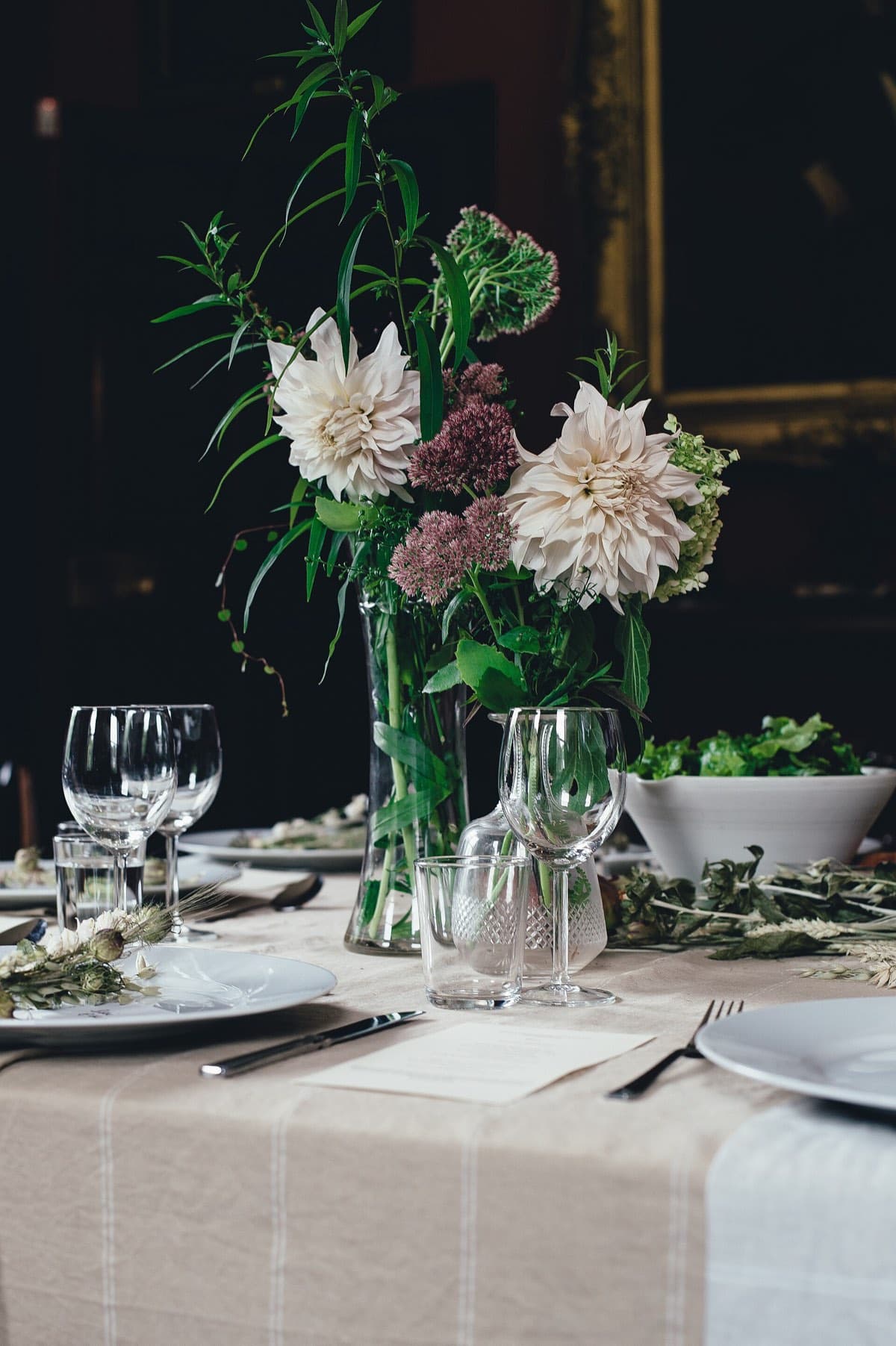 A dinner table with a bouquet of flowers and glasses in low light