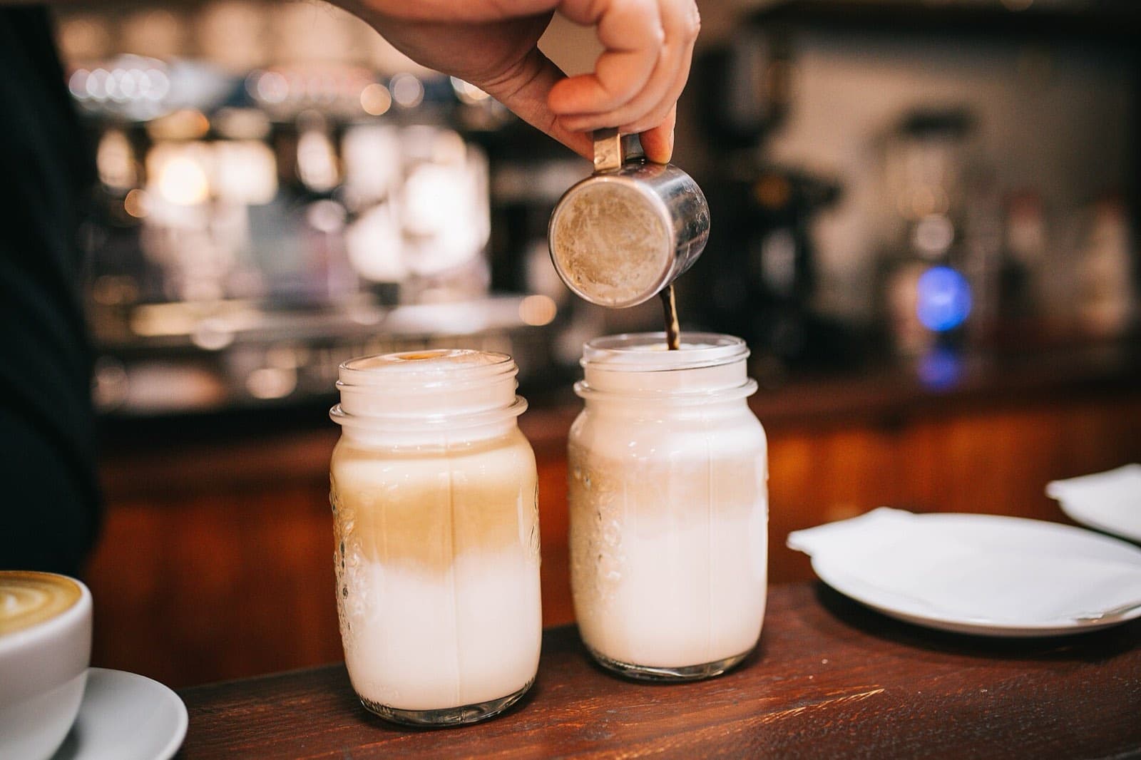 A barista pouring coffee into glass jars of milk
