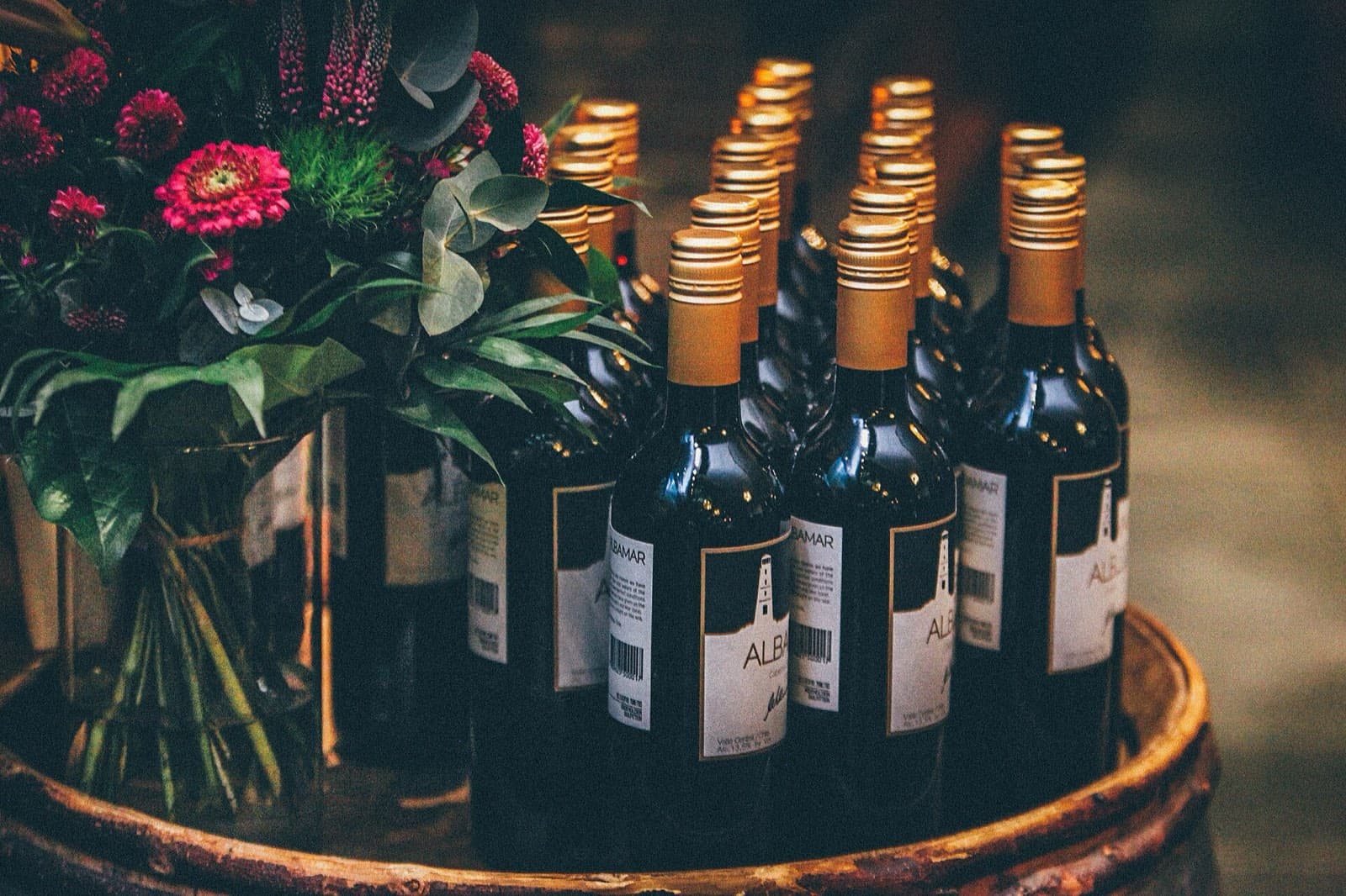 Wine bottles in a wooden barrel beside fresh flowers
