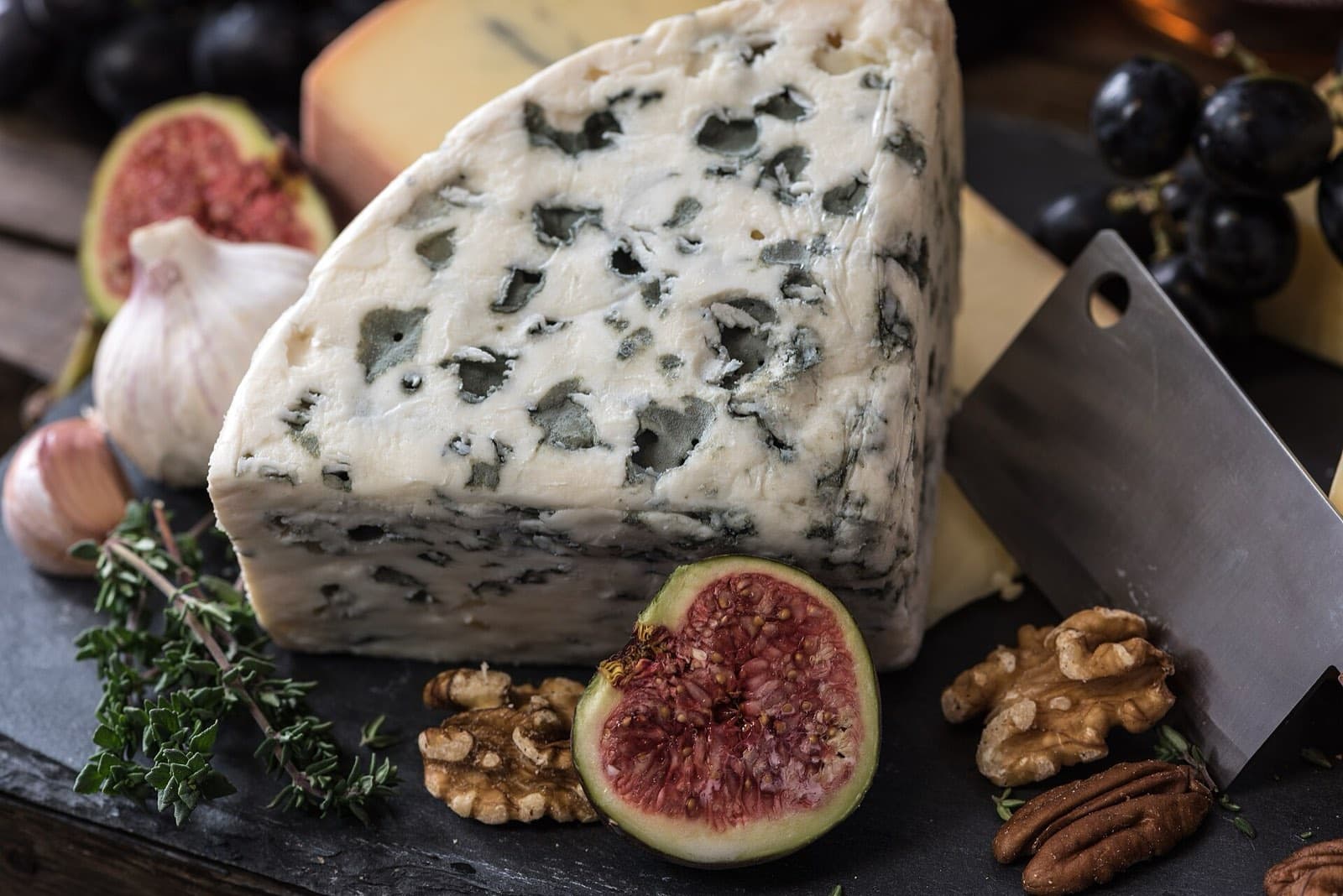 A wedge of blue cheese with figs, nuts and herbs on a dark board