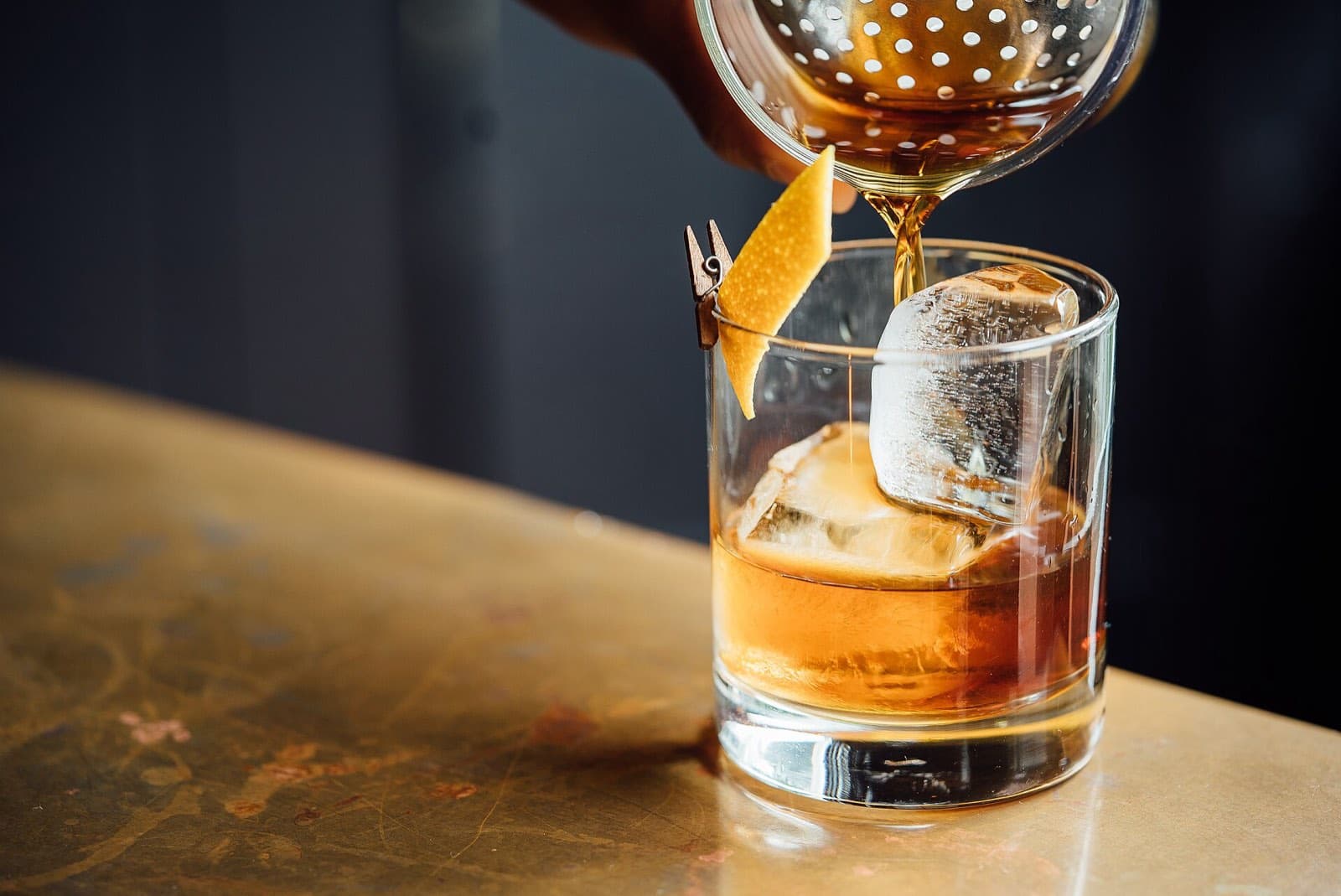 A cocktail being strained over a large ice cube