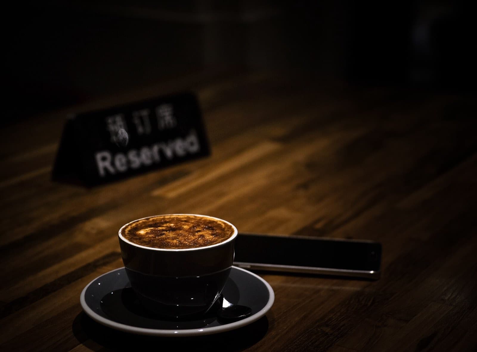 An espresso beside a small reserved sign on a dark wooden table