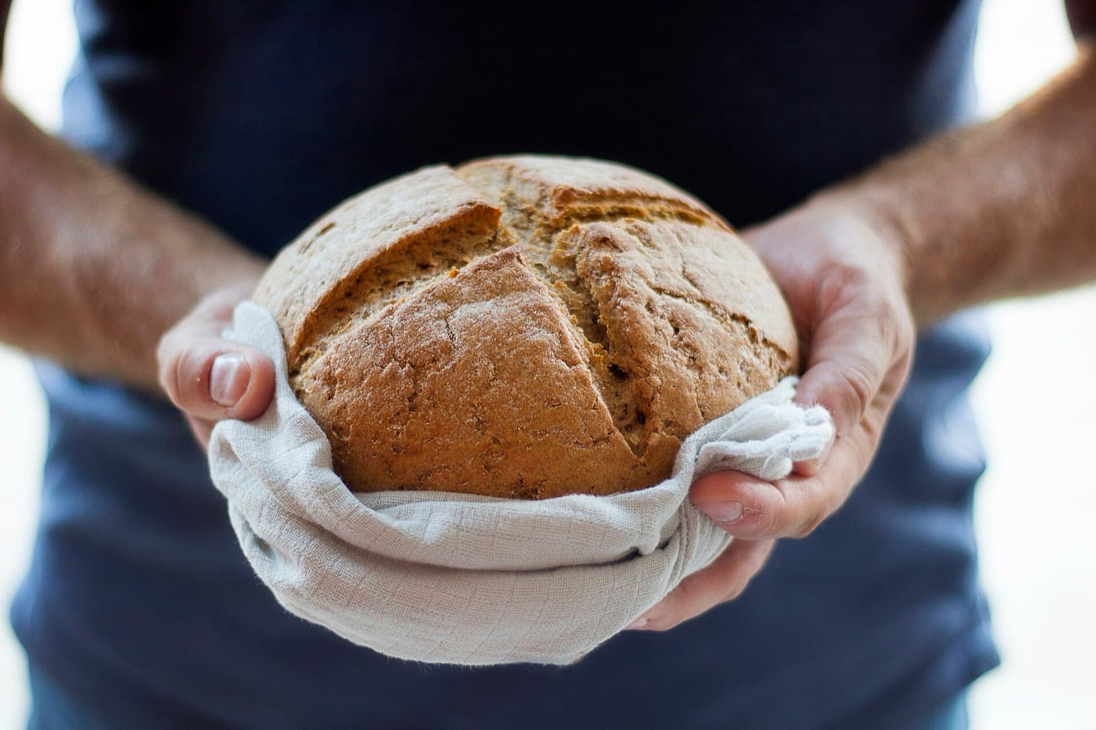 Hands holding a round sourdough loaf wrapped in a cloth