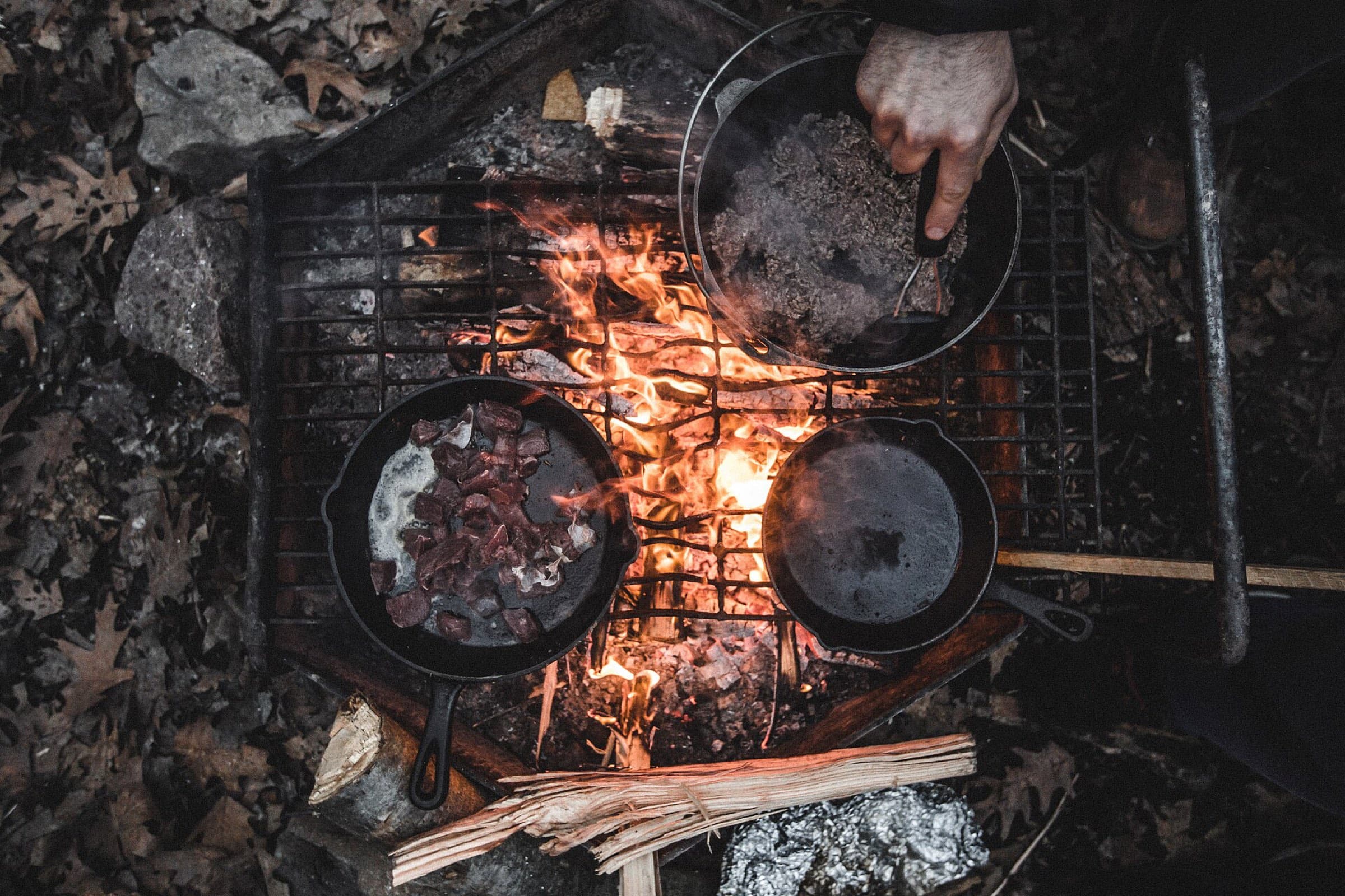 Cast-iron pans cooking over an open wood fire, seen from above