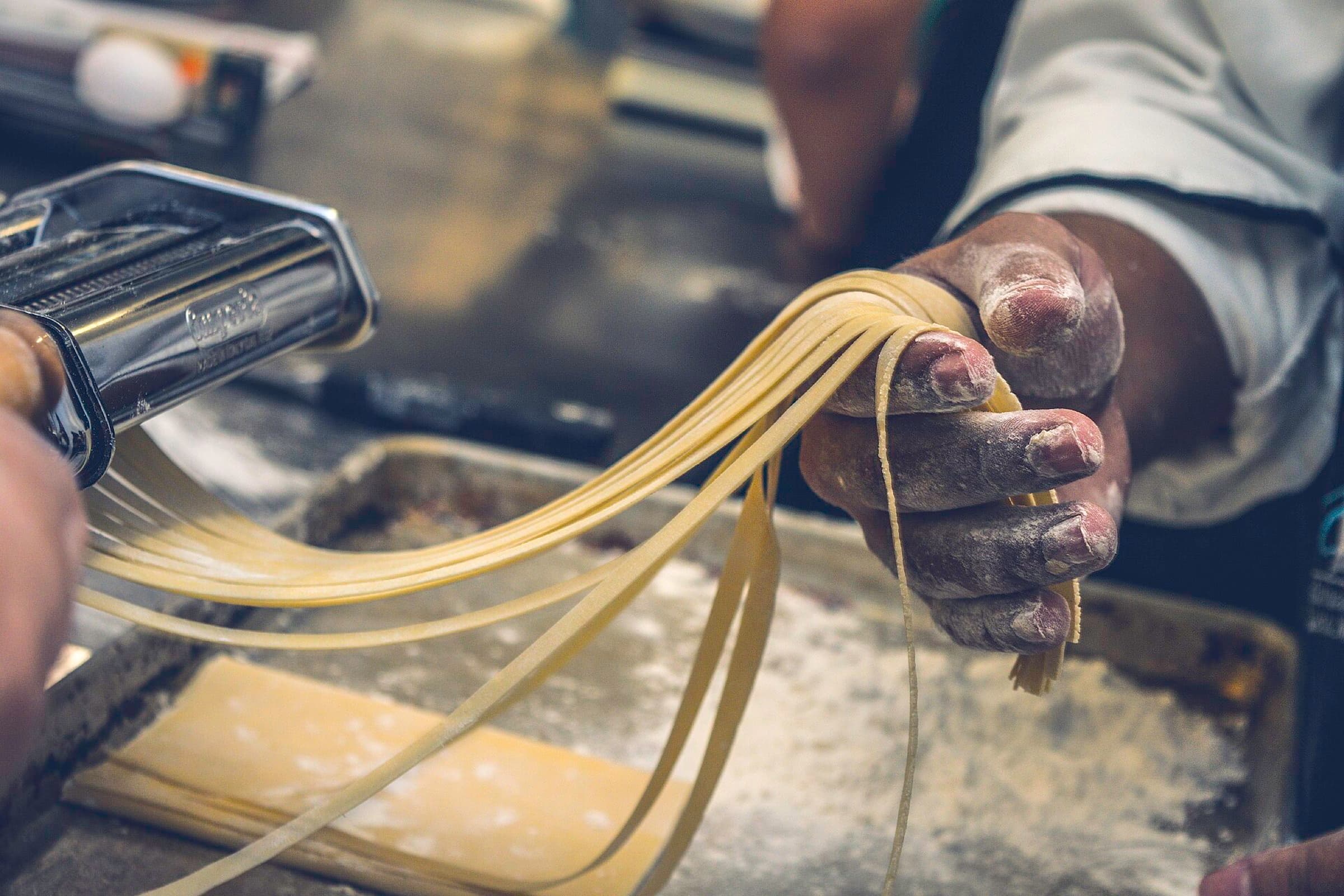 Hands guiding fresh pasta strands out of a pasta machine