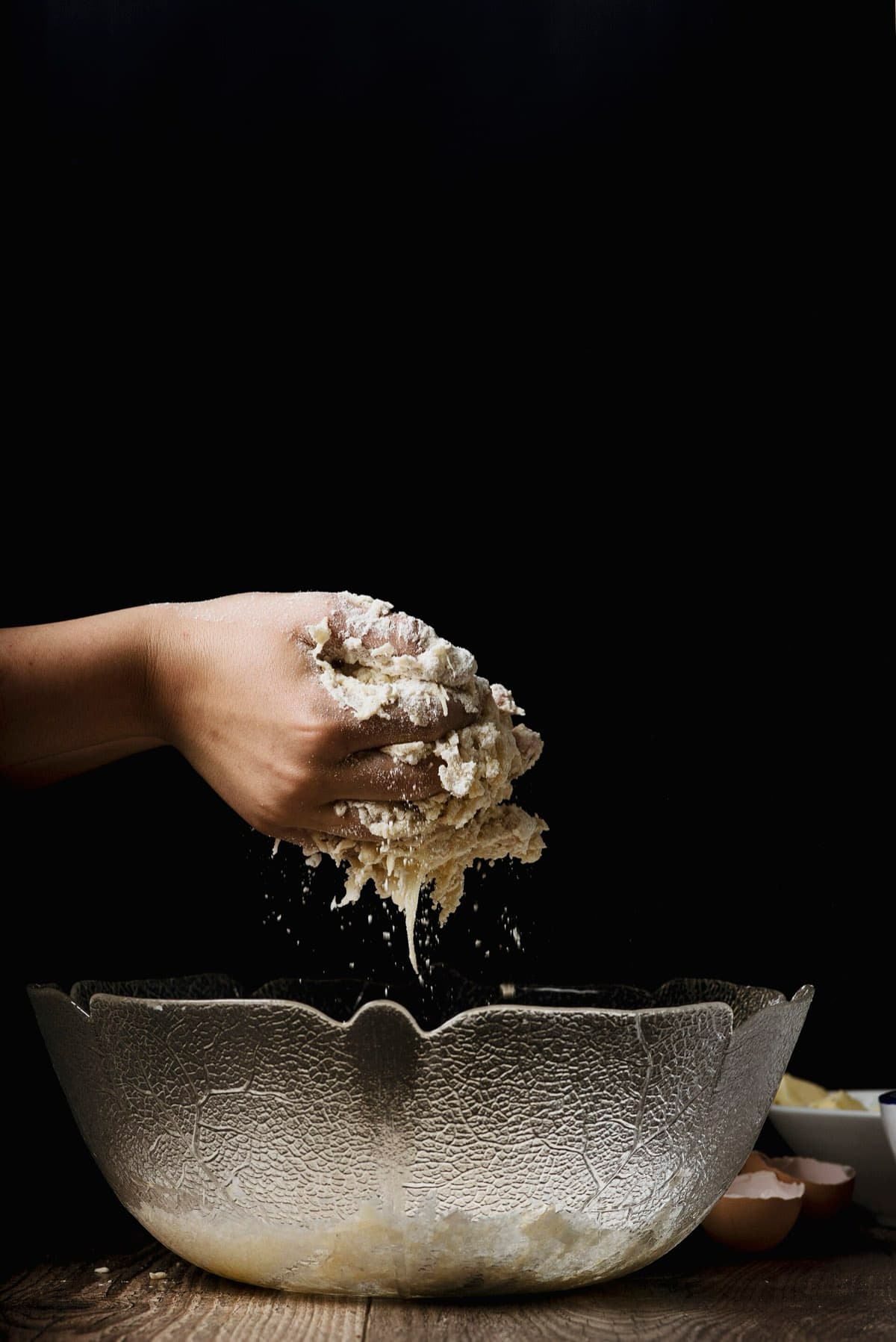 A hand dusting flour over a glass bowl against a dark background