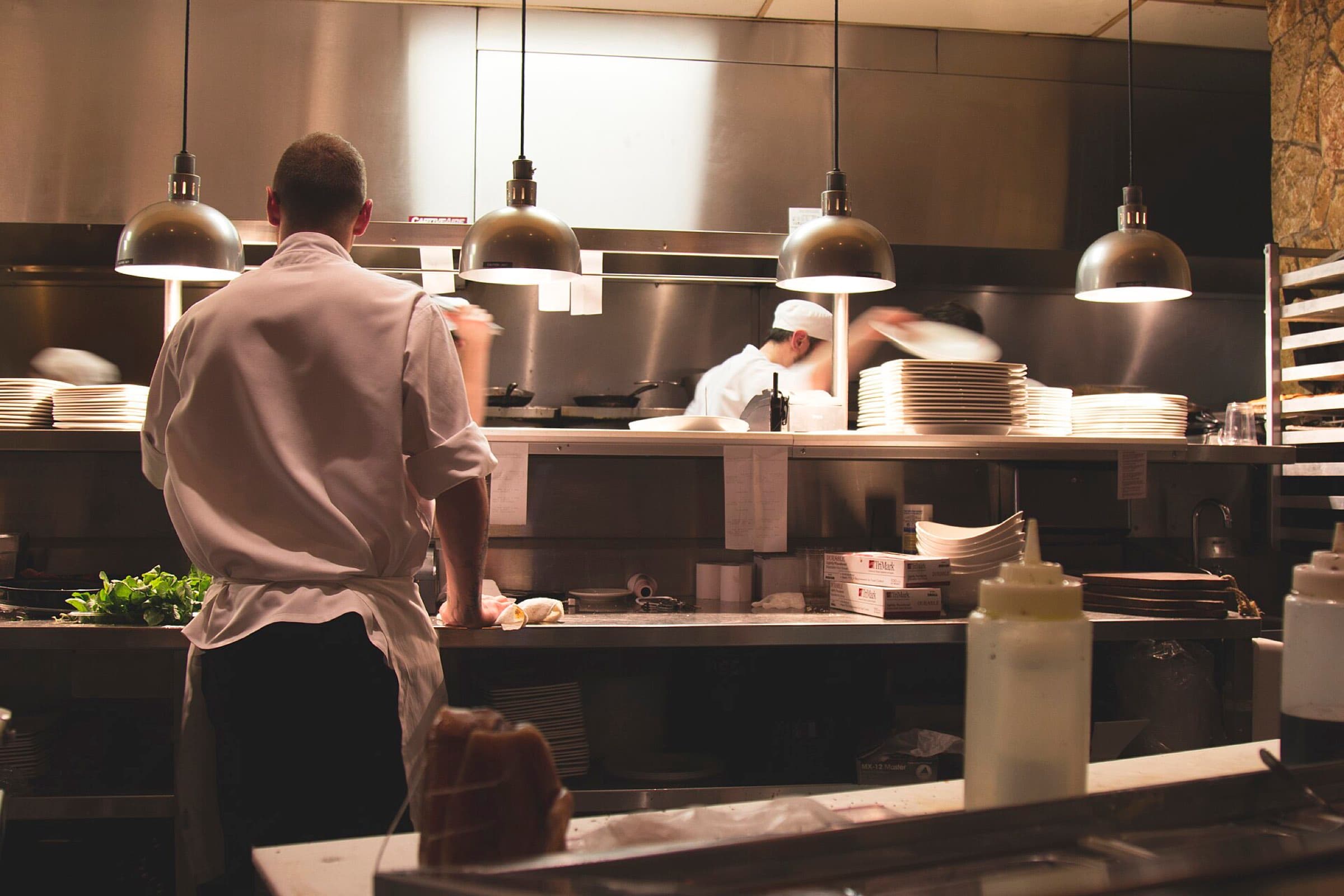 A chef working in an open kitchen under hanging pendant lamps