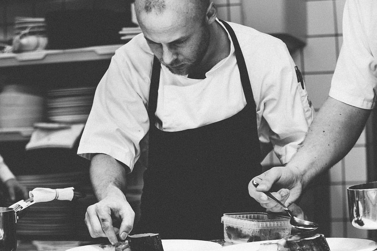 A chef in an apron carefully plating a dish, in black and white