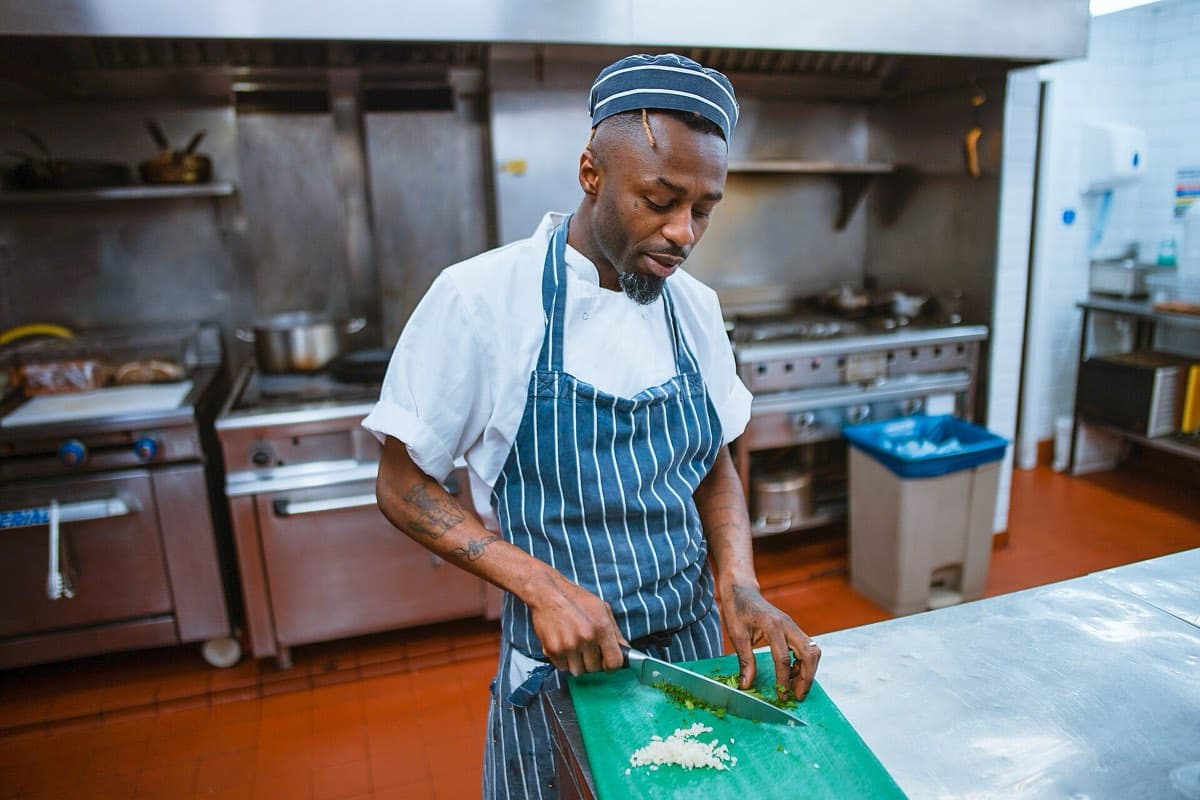 A chef in a striped apron chopping vegetables in a professional kitchen